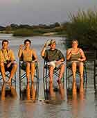 Group travel - travellers sitting on chairs in the river with sundowner drinks in a row